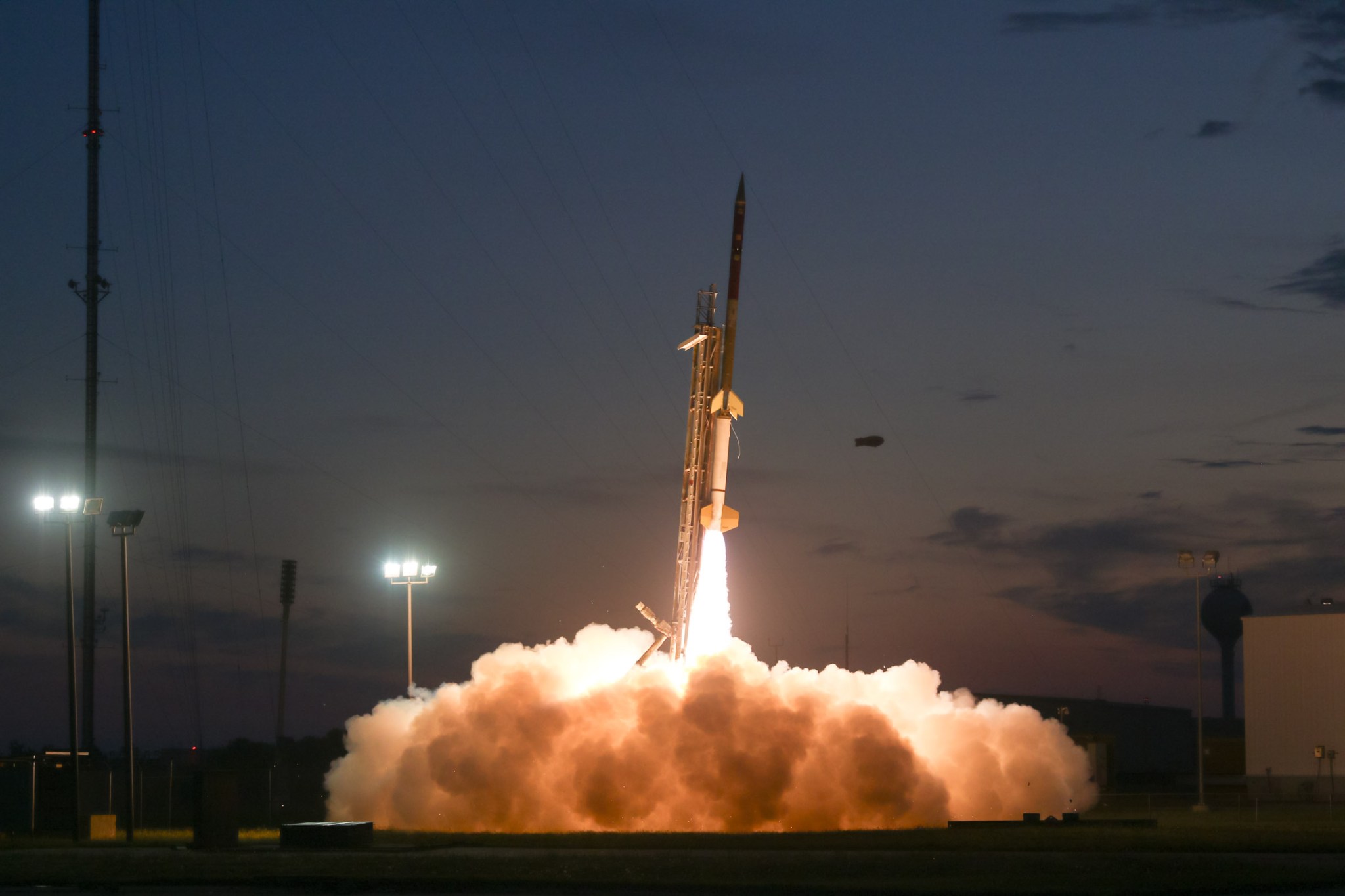 A rocket launching at dusk or dawn, with bright orange flames and billowing smoke at its base