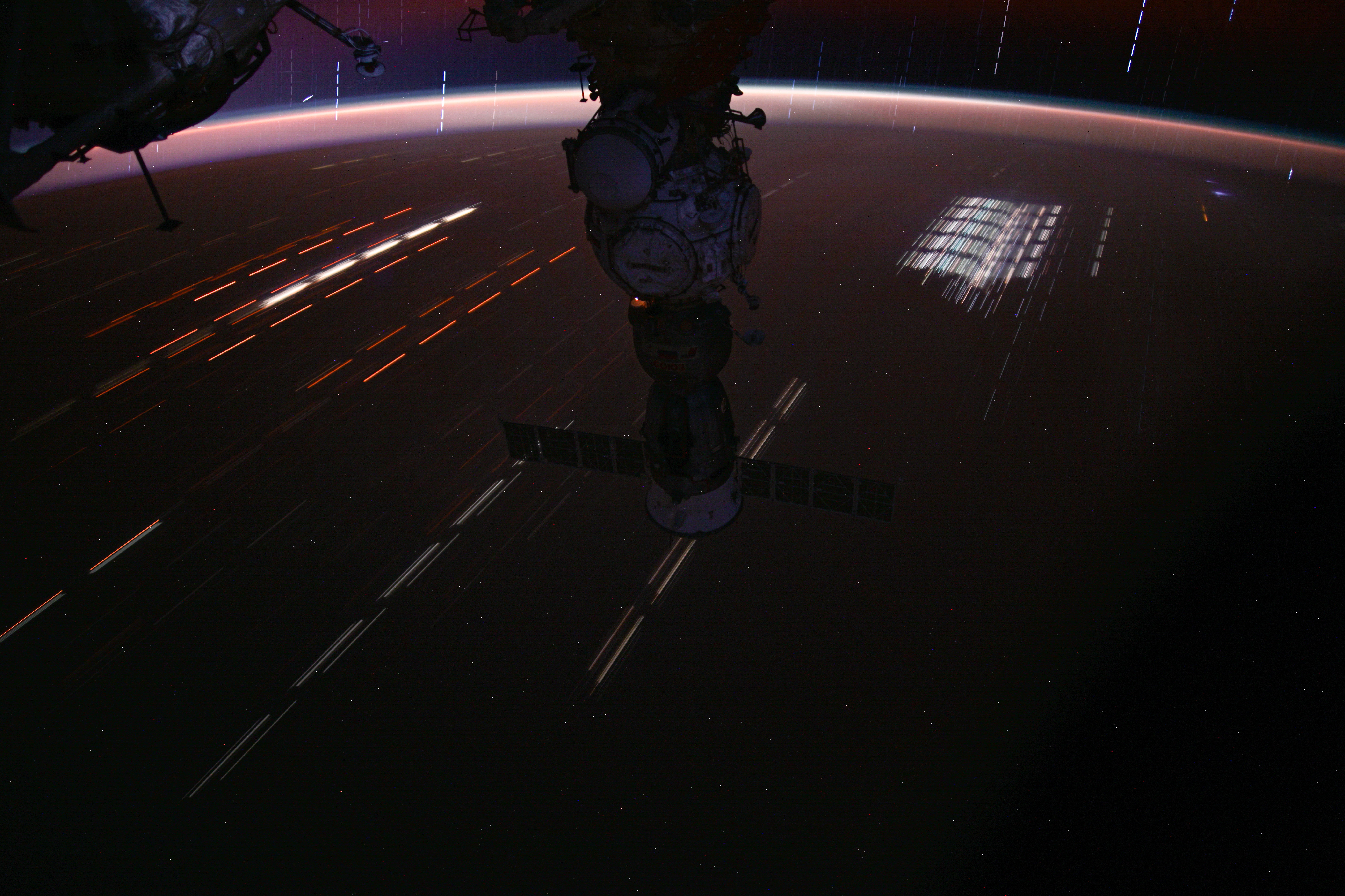 This long-duration photograph of the Soyuz MS-25 spacecraft with light trails on Earth below and stars trails above the horizon was taken by NASA astronaut Matthew Dominick as the International Space Station soared 262 miles above a sparsely populated region of Queensland, Australia.