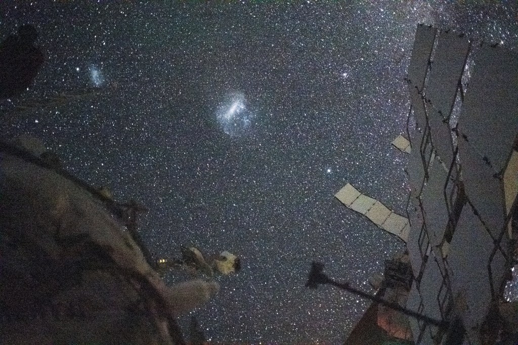 The Large Magellanic Cloud (center) and the Small Magellanic Cloud (upper left), dwarf galaxies in close proximity with the Milky Way galaxy, are pictured from the International Space Station. NASA astronaut and Expedition 71 Flight Engineer Matthew Dominick took this long-duration photograph with a station camera increasing its sensitivity to account for low light conditions.