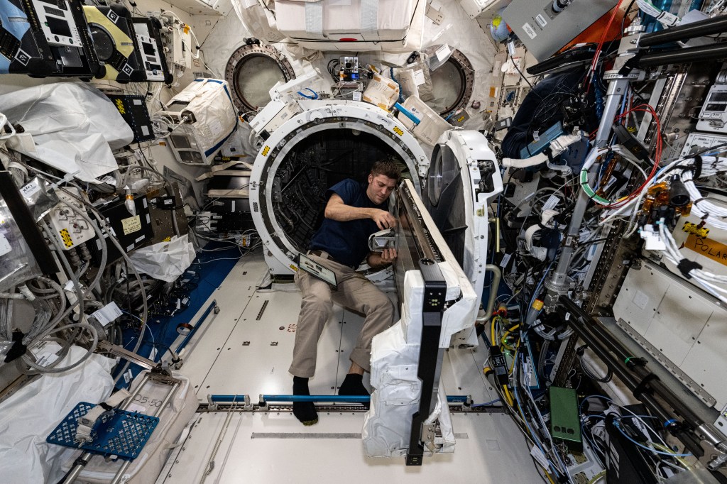 NASA astronaut and Expedition 71 Flight Engineer Matthew Dominick checks CubeSat configurations packed inside launch cases installed in the Kibo laboratory module's Small Satellite Orbital Deployer.