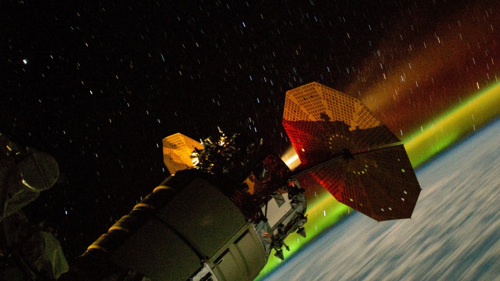 This long-duration photograph taken with a station camera uses increased sensitivity and shows the Northrop Grumman Cygnus space freighter firing its engine to raise the International Space Station's orbital altitude. The reboosts counteract atmospheric drag and prepare for the space station upcoming spacecraft activities. The orbital outpost was soaring 263 miles above the Indian Ocean with a field of star trails above and the Aurora Australis below.