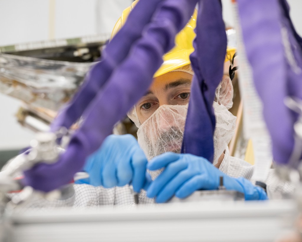 A person wears gloves, a hat, and a face mask while working on a piece of equipment.
