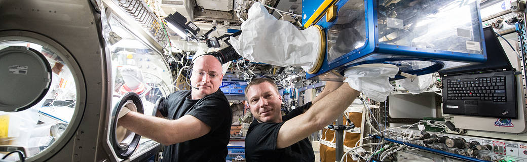 Two astronauts on ISS with their hands in glove boxes