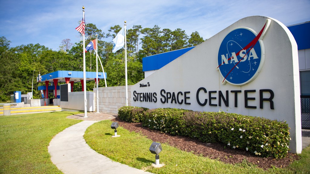 a view of the South Gate at Stennis Space Center is captured with the American, state and NASA flags flying and the guard shed in the background