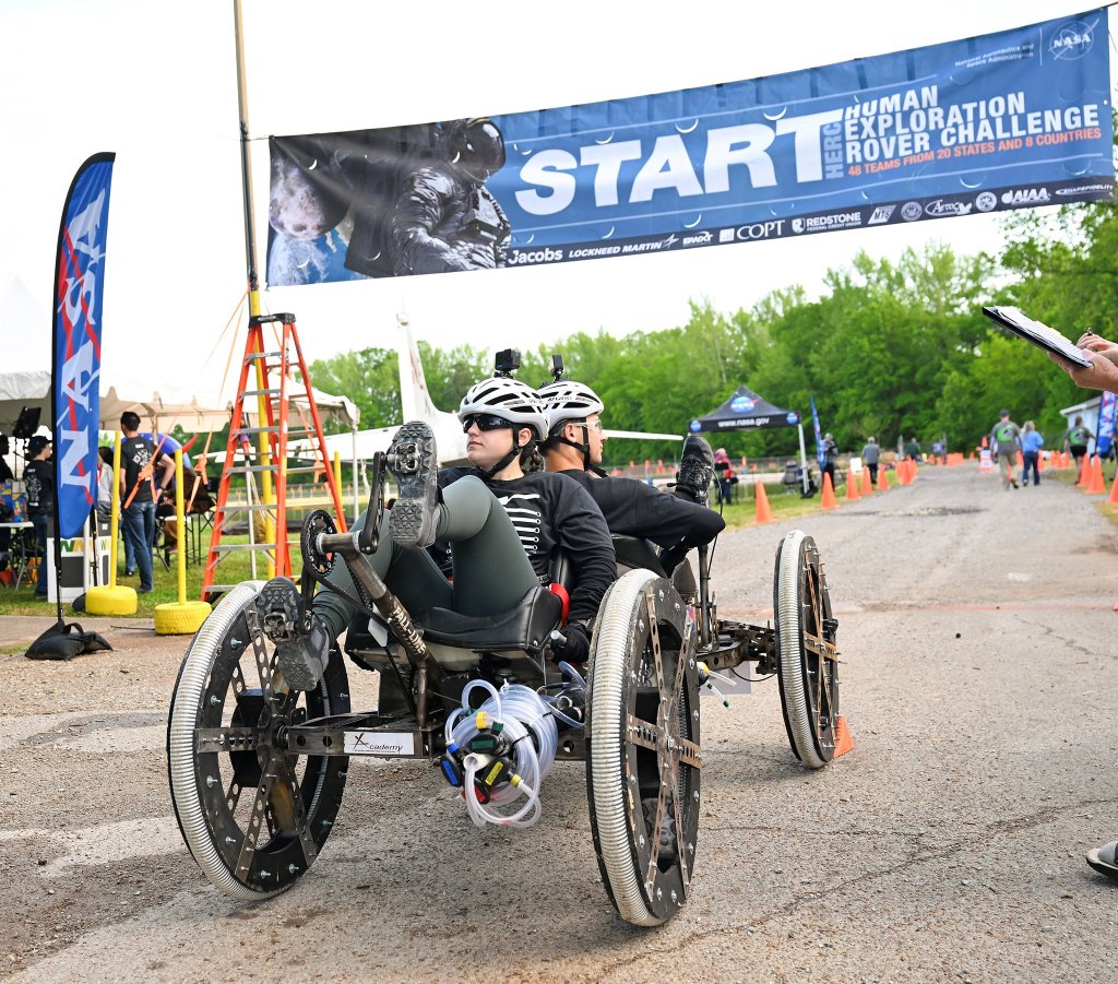 Two people on a rover challenge vehicle with a Start the challenge banner hanging above