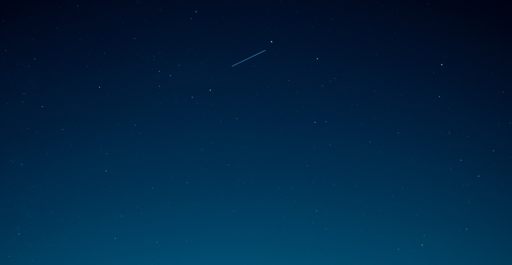 A view of point stars in the evening sky with a bright streak of light near the top of the photo.