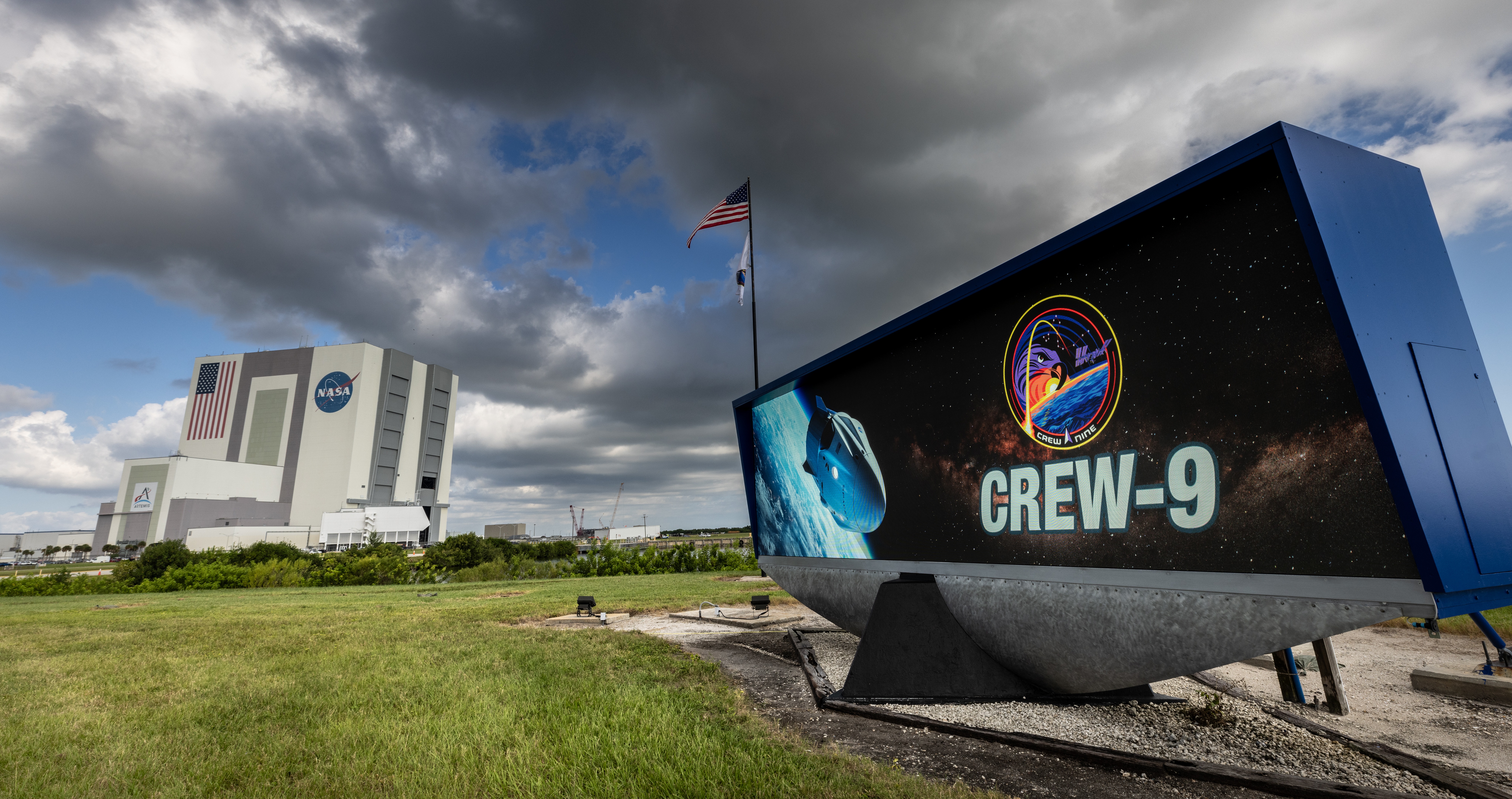 Image shows NASA's SpaceX Crew-9 logo with the iconic Vehicle Assembly Building in the background at NASA's Kennedy Space Center