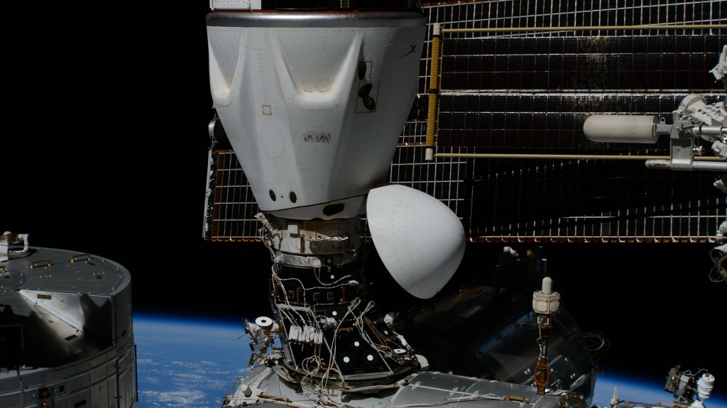 The SpaceX Dragon Endeavour spacecraft is pictured docked to the International Space Station's space-facing port on the Harmony module. Behind Dragon is a pair of main solar arrays fronted by a smaller roll-out solar array augmenting the orbital outpost's power generation system.
