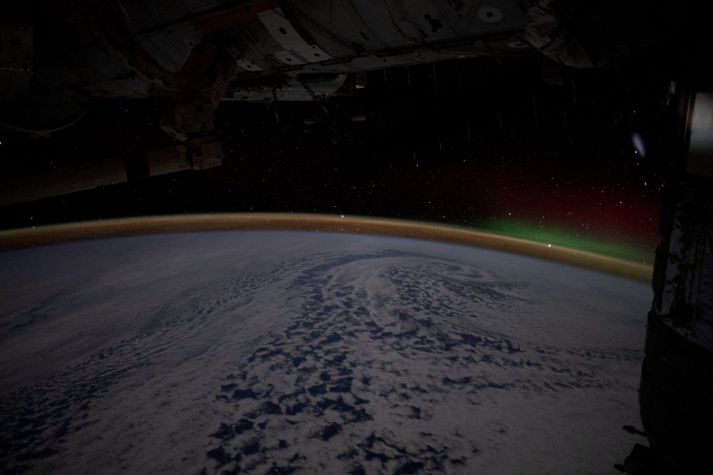 A wispy aurora australis rises above Earth's airglow blanketing the horizon in this long-duration photograph from the International Space Station as it orbited 270 miles above the Pacific Ocean southeast of New Zealand.