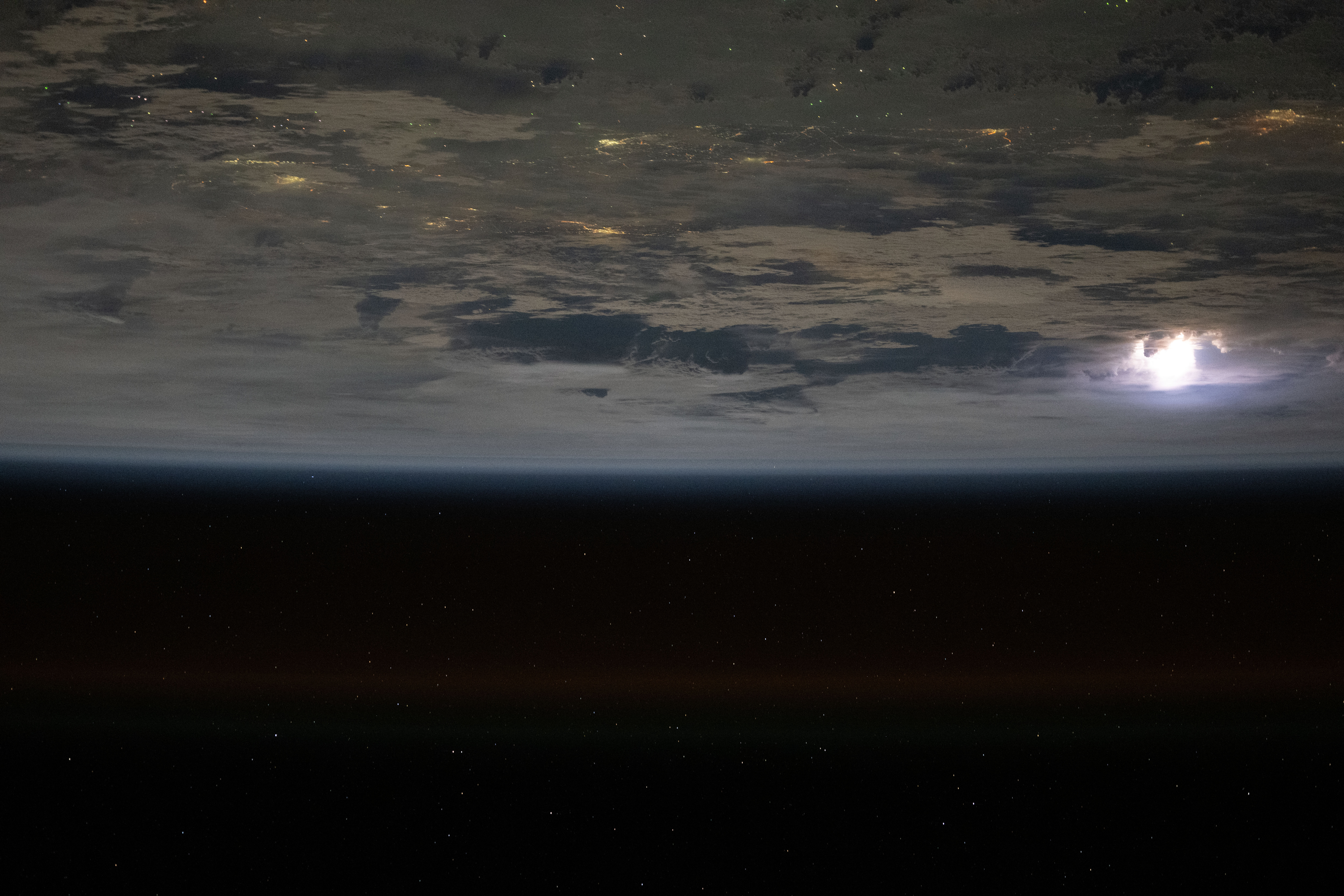 Lightning (at right) illuminates the clouds in this photograph from the International Space Station as it orbited 261 miles above the South China Sea with the city lights of Southeast Asia shining through.