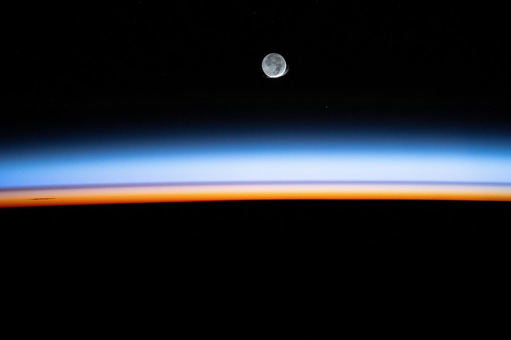 The New Moon begins setting above Earth's bright, colorful atmosphere in this long-duration photograph taken by NASA astronaut Matthew Dominick with a camera programmed for high sensitivity aboard the International Space Station.