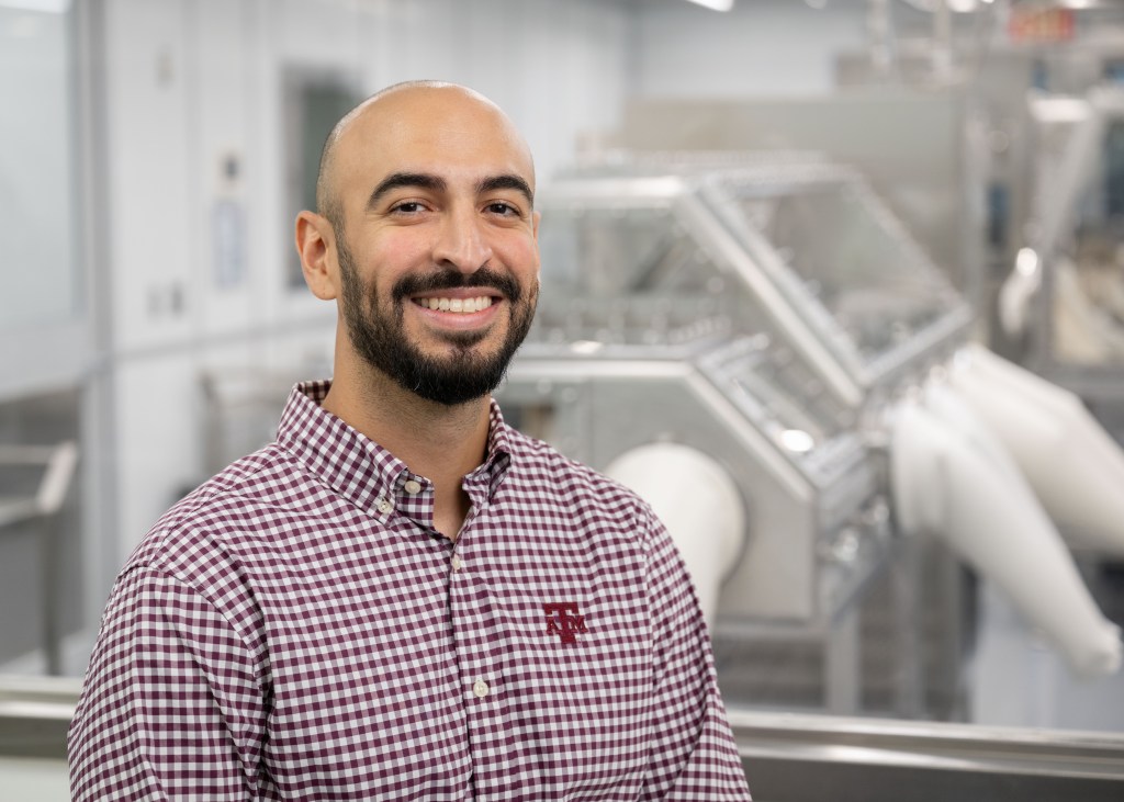 Lead Astromaterial Curation Engineer Salvador Martinez III smiles at the camera wearing a plaid shirt inside the OSIRIS REx Lab.