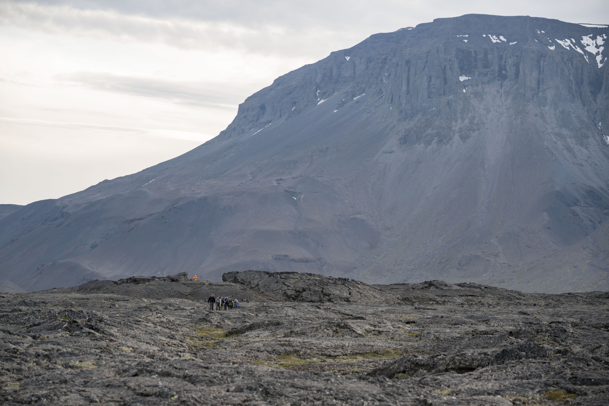 A large scenic view of a mountain. In the bottom left, small silhouettes of people.