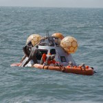 Wearing Biological Isolation Garments and assisted by a decontamination officer, standing in the open hatch, Apollo 12 astronauts await retrieval in the life raft