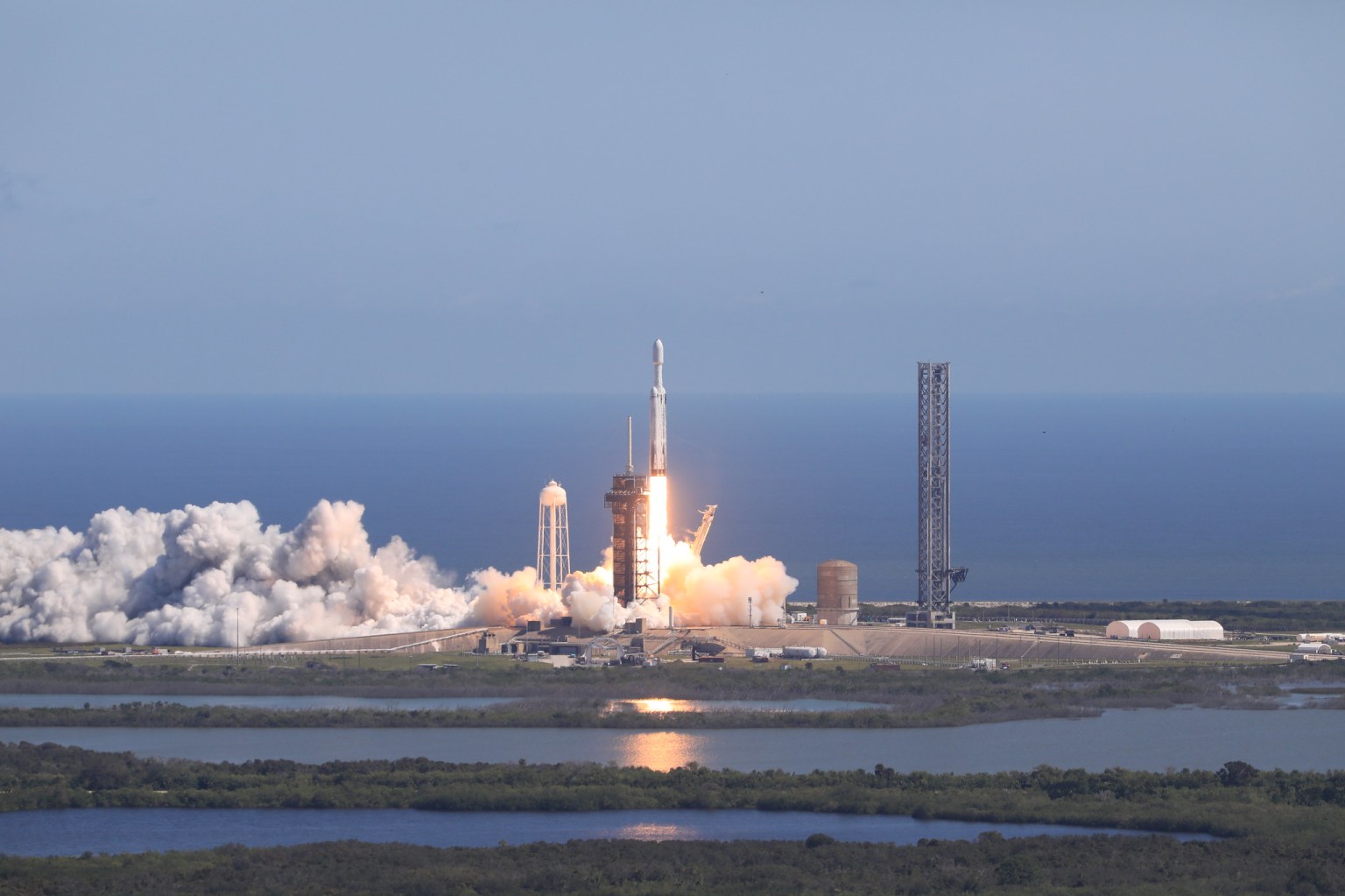 A SpaceX Falcon Heavy rocket carrying NASA’s Europa Clipper spacecraft launches off the coast of Florida, with blue skies and ocean in the background.