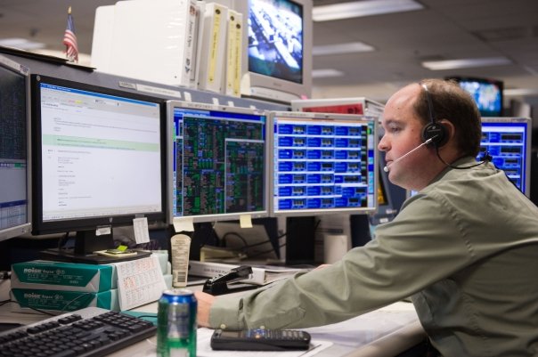 Jesse Bazley sits at a console in the Mission Control Center, wearing a headset.