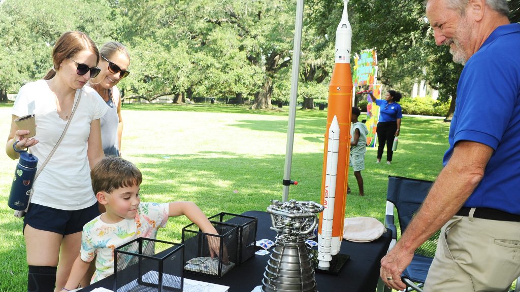 A young boy visits the coloring station while attending NASA Day at the Audubon Zoo in New Orleans while NASA representative Lacy Thompson looks on with an encouraging smile.