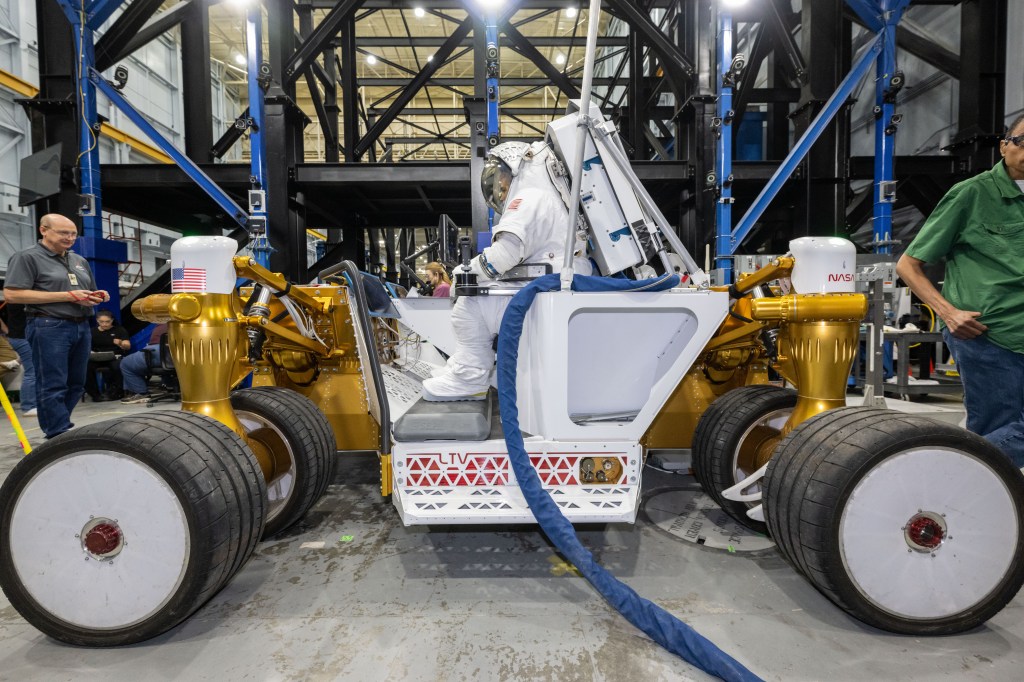 A suited NASA engineer sits on the agency’s rover prototype during testing at NASA’s Johnson Space Center in Houston.
