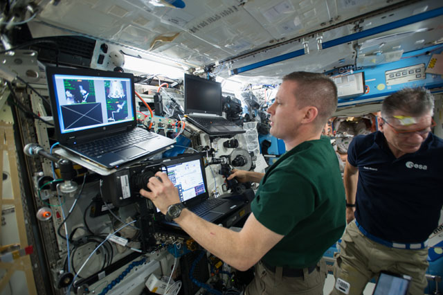 Two astronauts work on a complex system of laptops and instruments aboard the International Space Station.