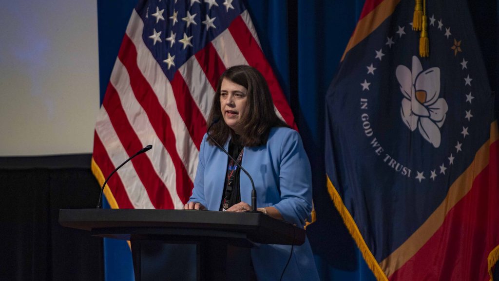 Christine Powell wearing a blue blazer stands in front of both the US and State of MS flags