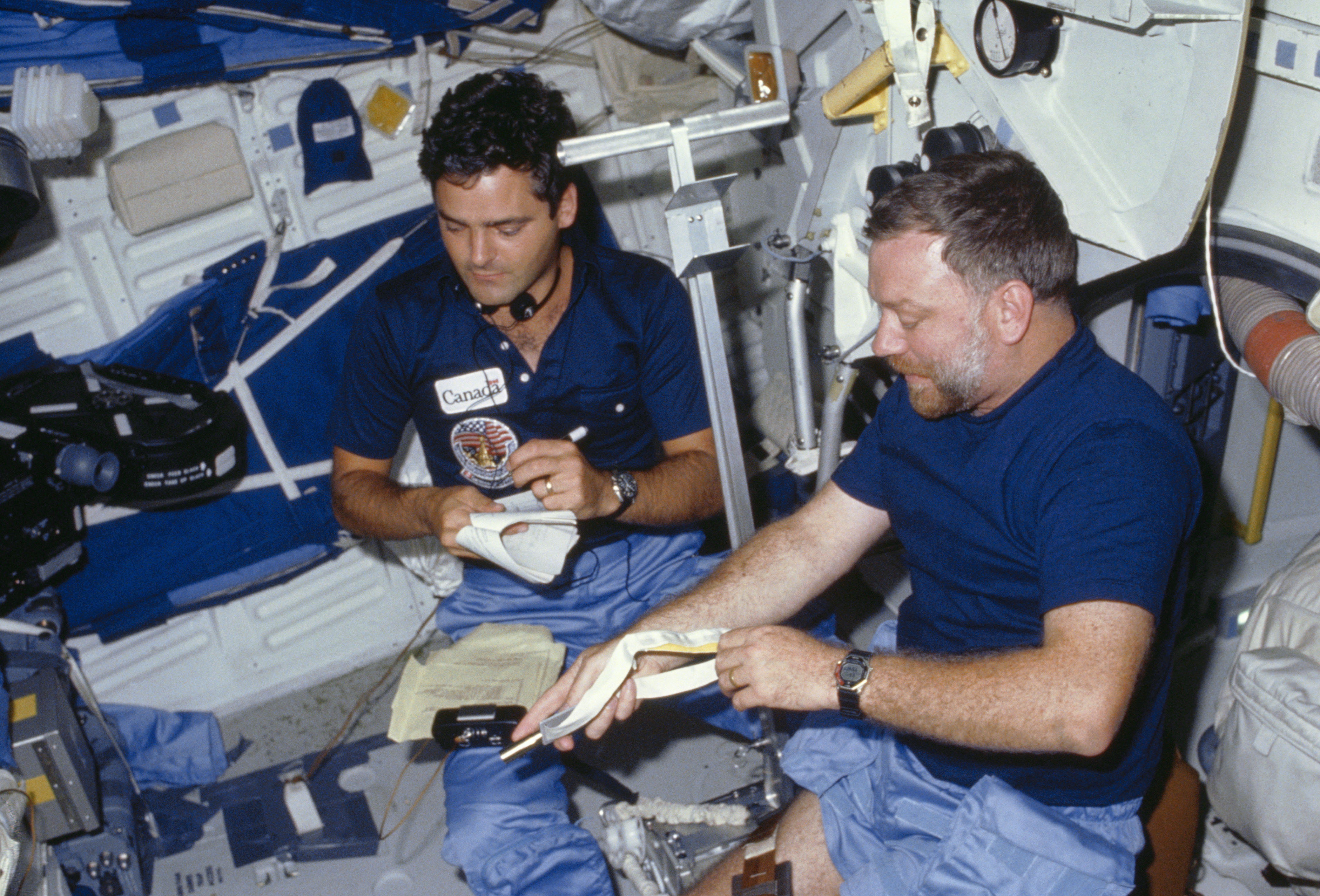 Payload Specialists Marc Garneau and Paul D. Scully-Power working on a Canadian experiment in Challenger’s middeck