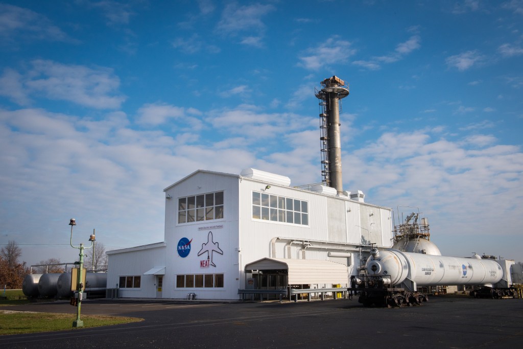 A white building surrounded by external equipment in front of a blue sky with clouds