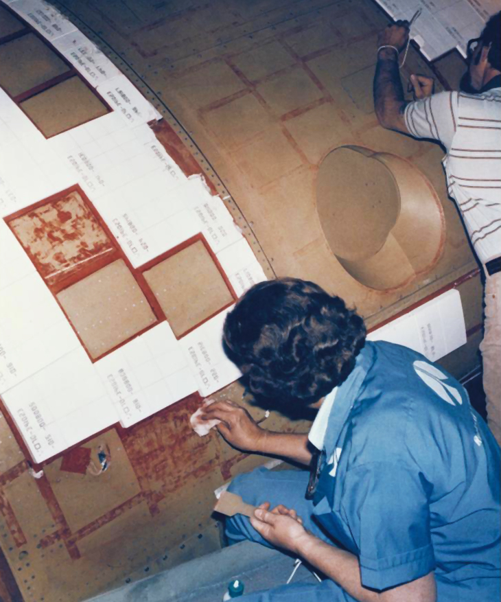 A worker applies ceramic tiles to the space shuttle.