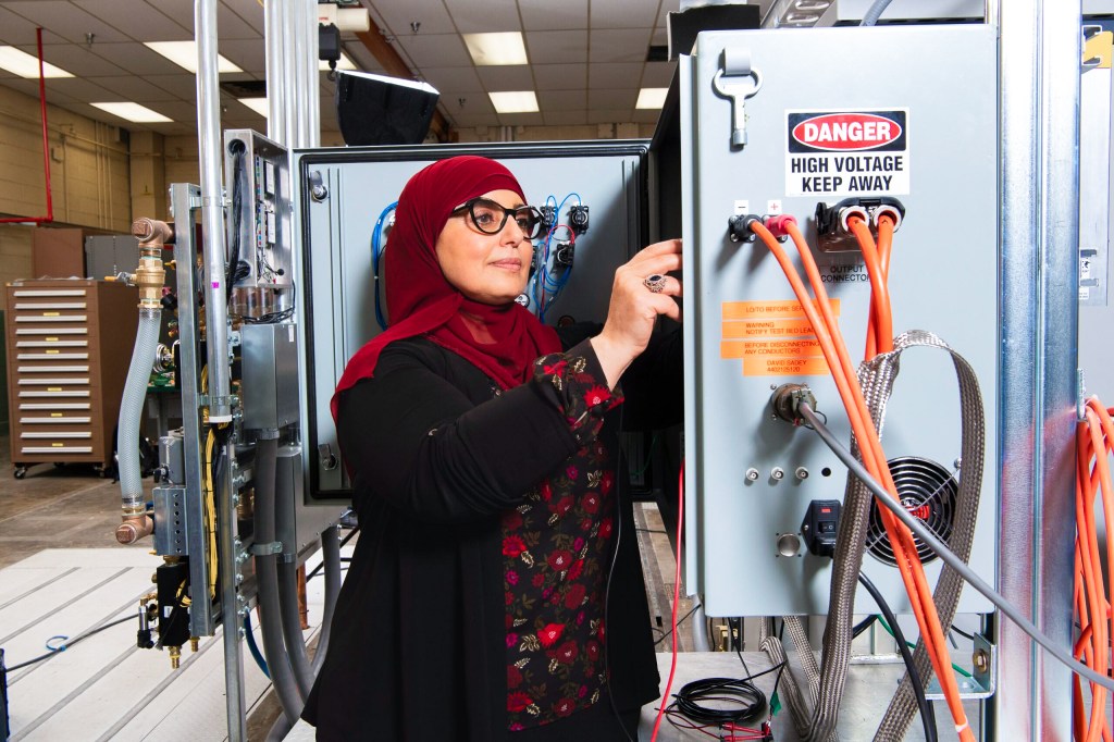A woman accesses the inside of a testing machine connected to wires inside the facility.