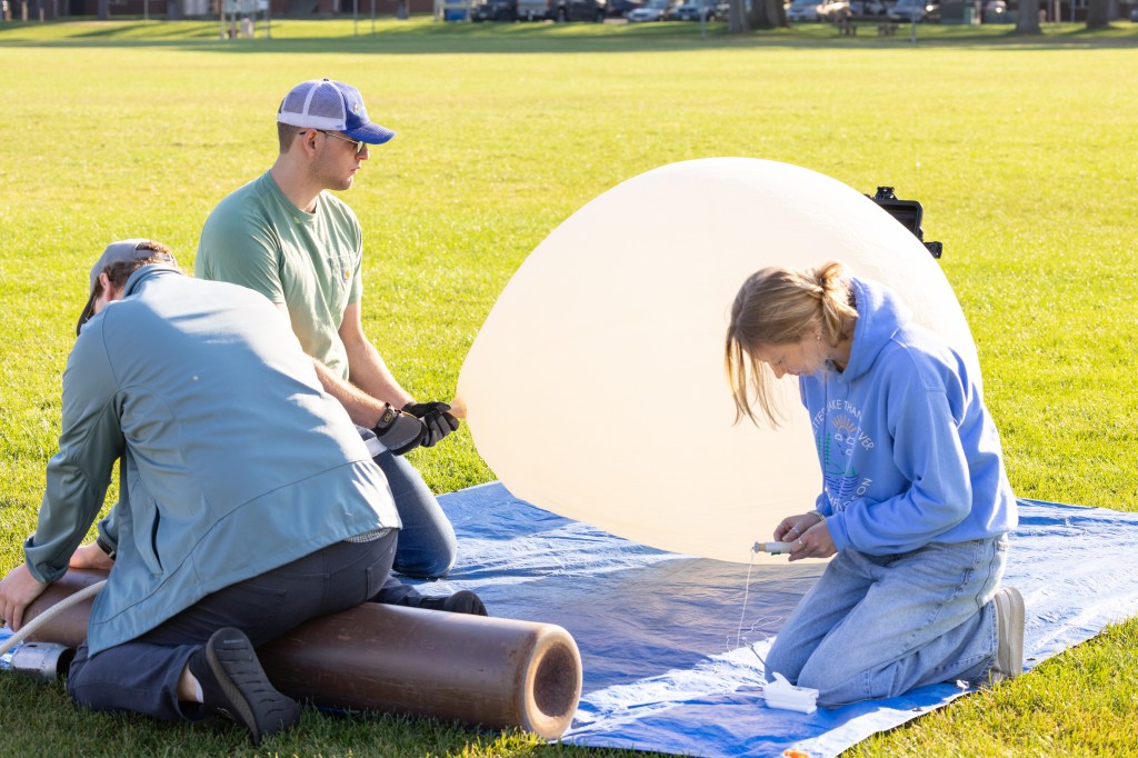 (From left) Cole Long, Logan Kearney, and Caeley Hodges from the University of Idaho inflate a weather balloon for launch, during FireSense’s uncrewed aerial system (UAS) technology demonstration in Missoula, Montana. These balloons use a sensor called a radiosonde to gather data on wind speed and direction.
