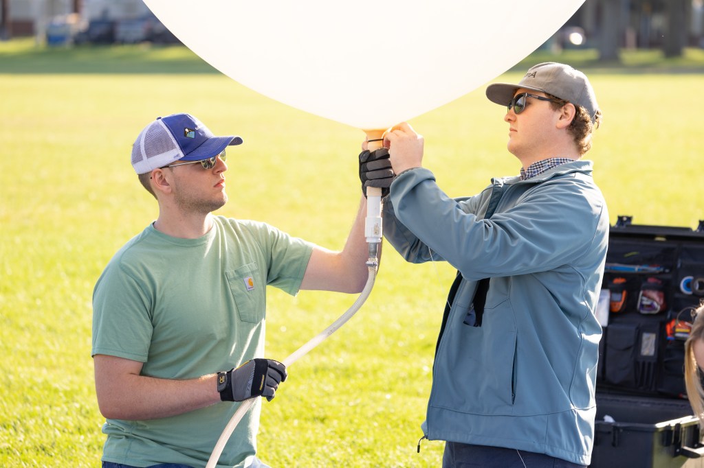 Logan Kearney and Cole Long, students at the University of Idaho, prepare a weather balloon for launch, during FireSense’s uncrewed aerial system (UAS) technology demonstration in Missoula, Montana. These balloons use a sensor called a radiosonde to gather data on wind speed and direction.