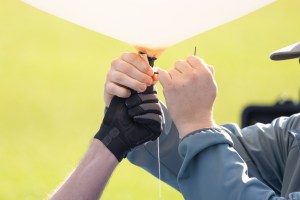 Logan Kearney and Cole Long, students at the University of Idaho, tie a zip tie to the base of a weather balloon as part of the preparations for launch, during FireSense’s uncrewed aerial system (UAS) technology demonstration in Missoula, Montana. These balloons use a sensor called a radiosonde to gather data on wind speed and direction.
