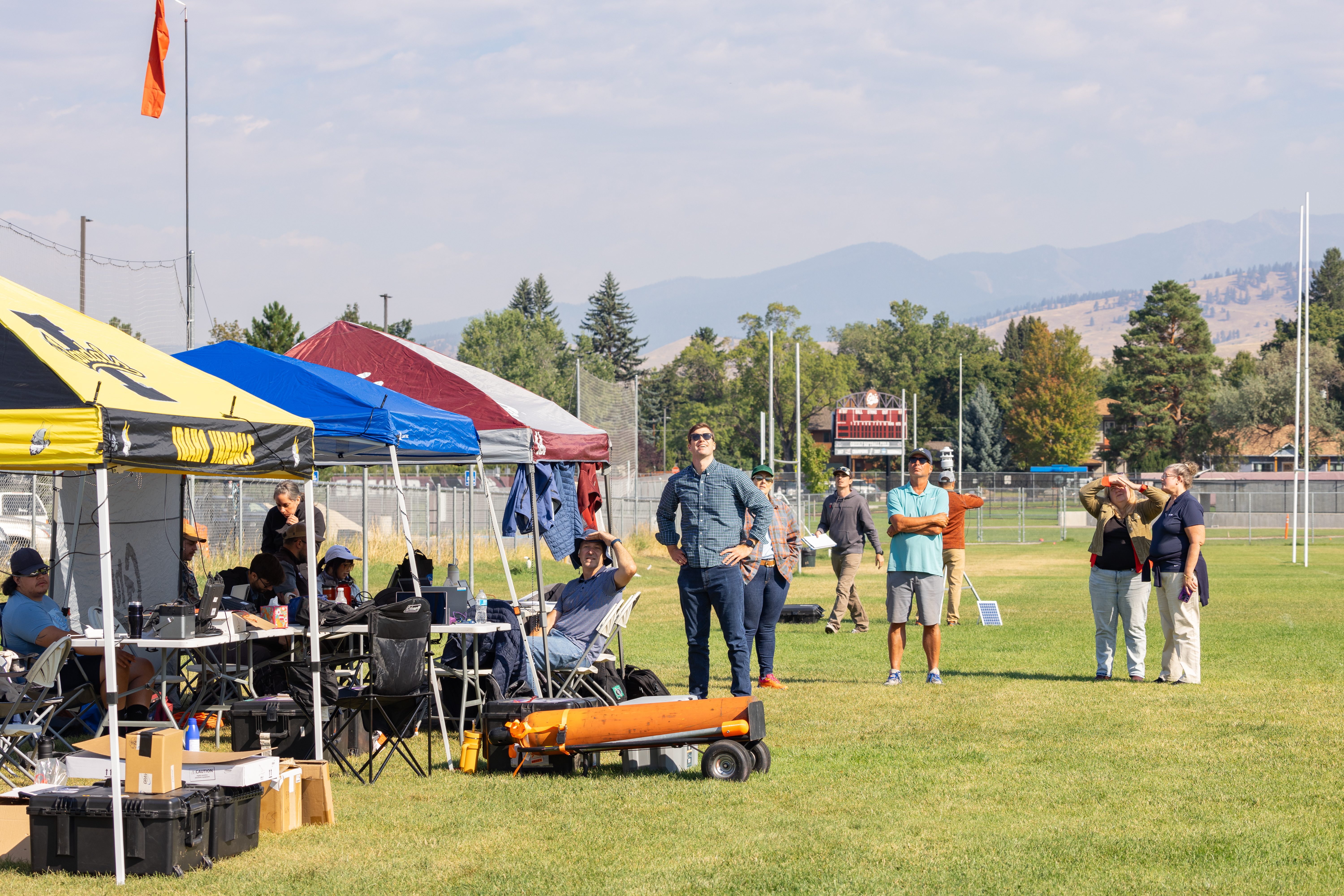 A field crew from MITRE, Esri, NASA, the University of Idaho, and Salish Kootenai College watch the NASA Alta X quadcopter rise into the air for its first flight of the FireSense uncrewed aerial system (UAS) technology demonstration in Missoula, Montana.