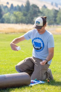 Steven Stratham, a student at Salish Kootenai College, attaches a sensor called a radiosonde to the string of a weather balloon during the FireSense uncrewed aerial system (UAS) technology demonstration in Missoula, Montana. The radiosonde will collect data on wind speed and direction and feed it back to the ground station.