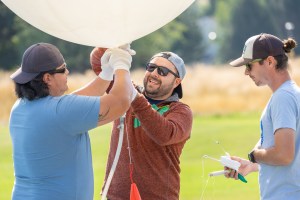 (From left) Travis Christopher, Danny Johnson, and Steven Stratham prepare a weather balloon for launch; Stratham holds a radiosonde sensor that will dangle under the balloon and gather data on wind speed and direction. This team from Salish Kootenai College is one of two teams that supported the FireSense UAS Technology Demonstration in Missoula, Montana.