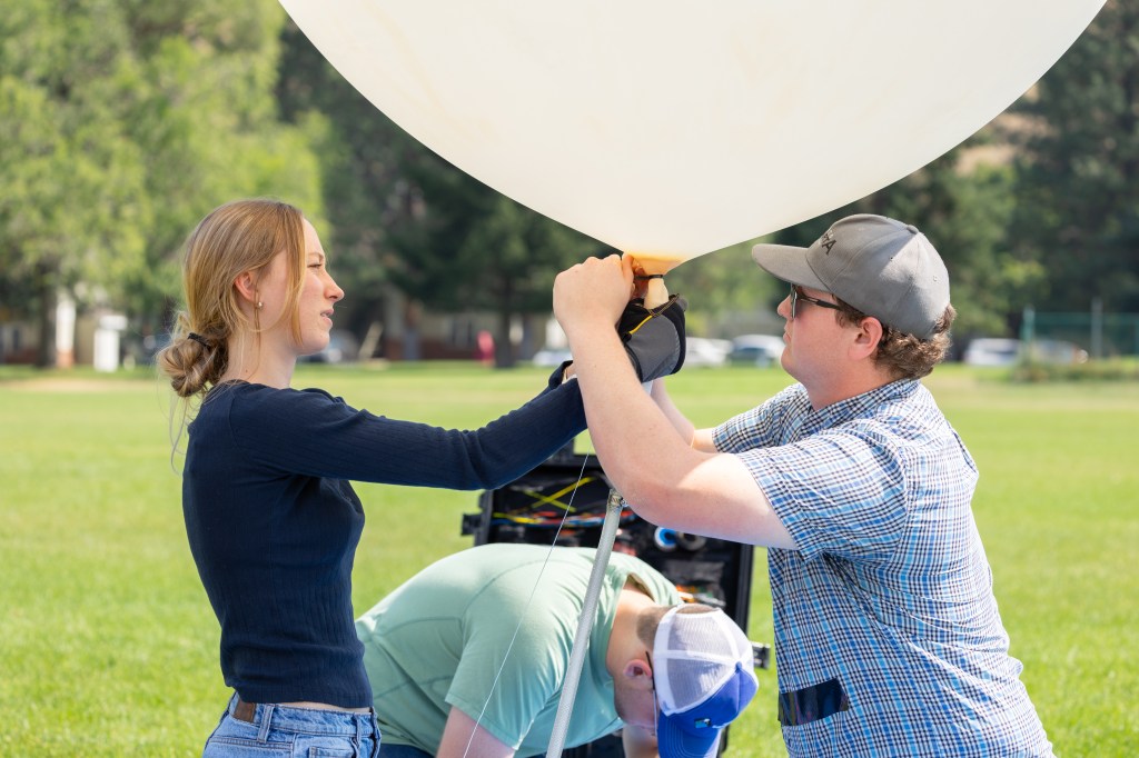 (From left) Caeley Hodges, Logan Kearney, and Cole Long, from the University of Idaho, tie off an weather balloon in preparation for launch during FireSense’s uncrewed aerial system (UAS) technology demonstration in Missoula, Montana. These balloons use a sensor called a radiosonde to gather data on wind speed and direction.