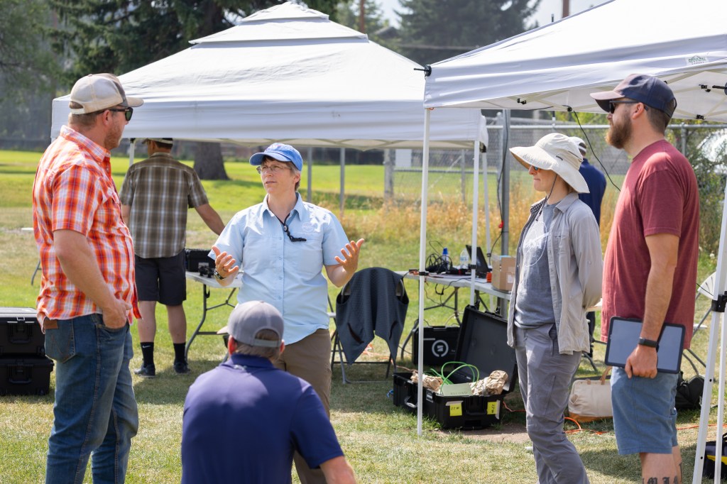 FireSense Project Manager Jennifer Fowler (center, blue hat) and FireSense Project Scientist Jacquelyn Shuman (second from right) speak with visitors from the US Forest Service, Region 1, during the FireSense uncrewed aerial system (UAS) Technology Demonstration in Missoula, Montana.