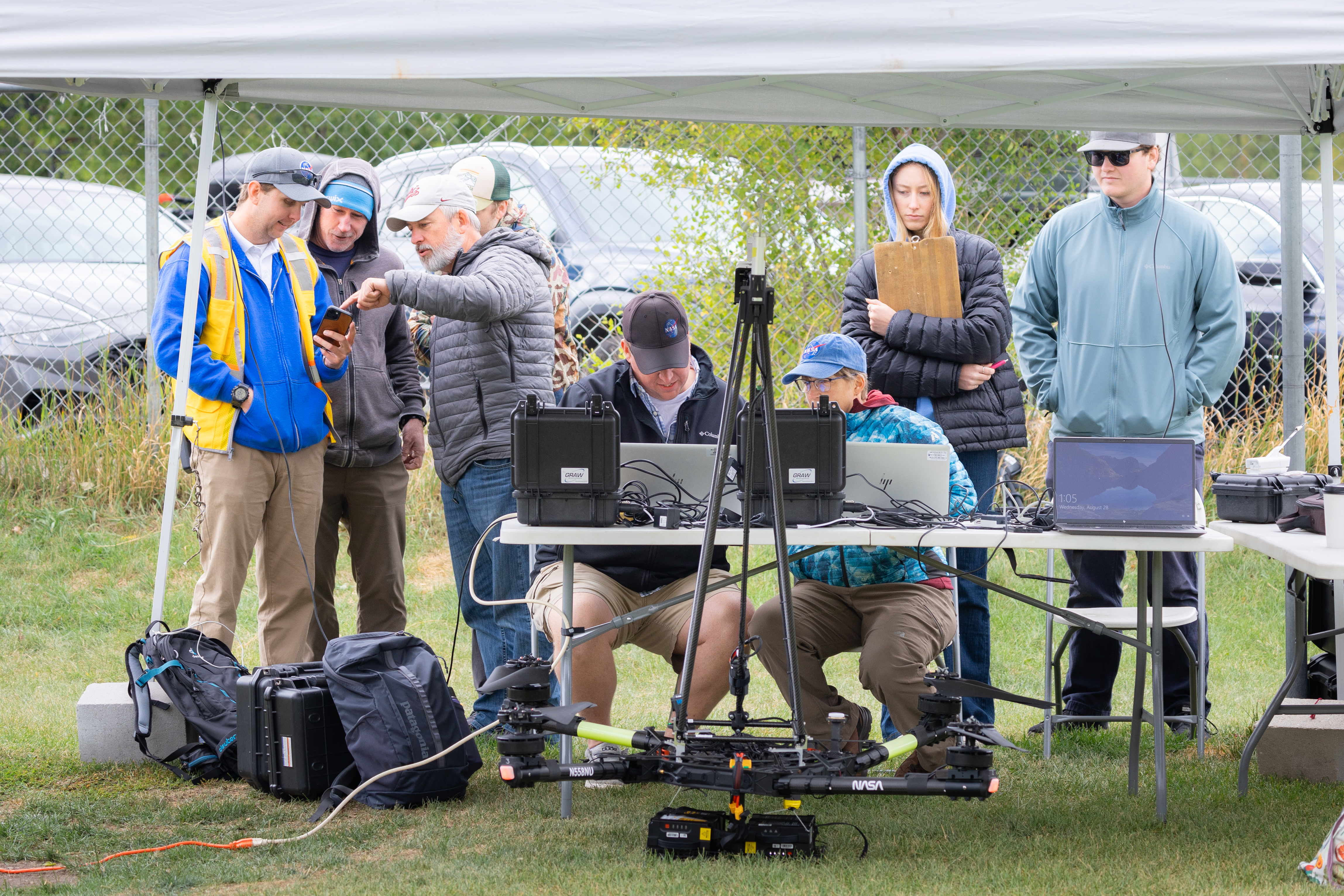 Team members from NASA and Salish Kootenai College stand in the control tent to watch the progress of the NASA Alta X quadcopter as it performs one of eight flights of the campaign.