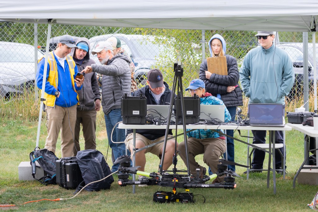 Team members from NASA and Salish Kootenai College stand in the control tent to watch the progress of the NASA Alta X quadcopter as it performs one of eight flights of the campaign.