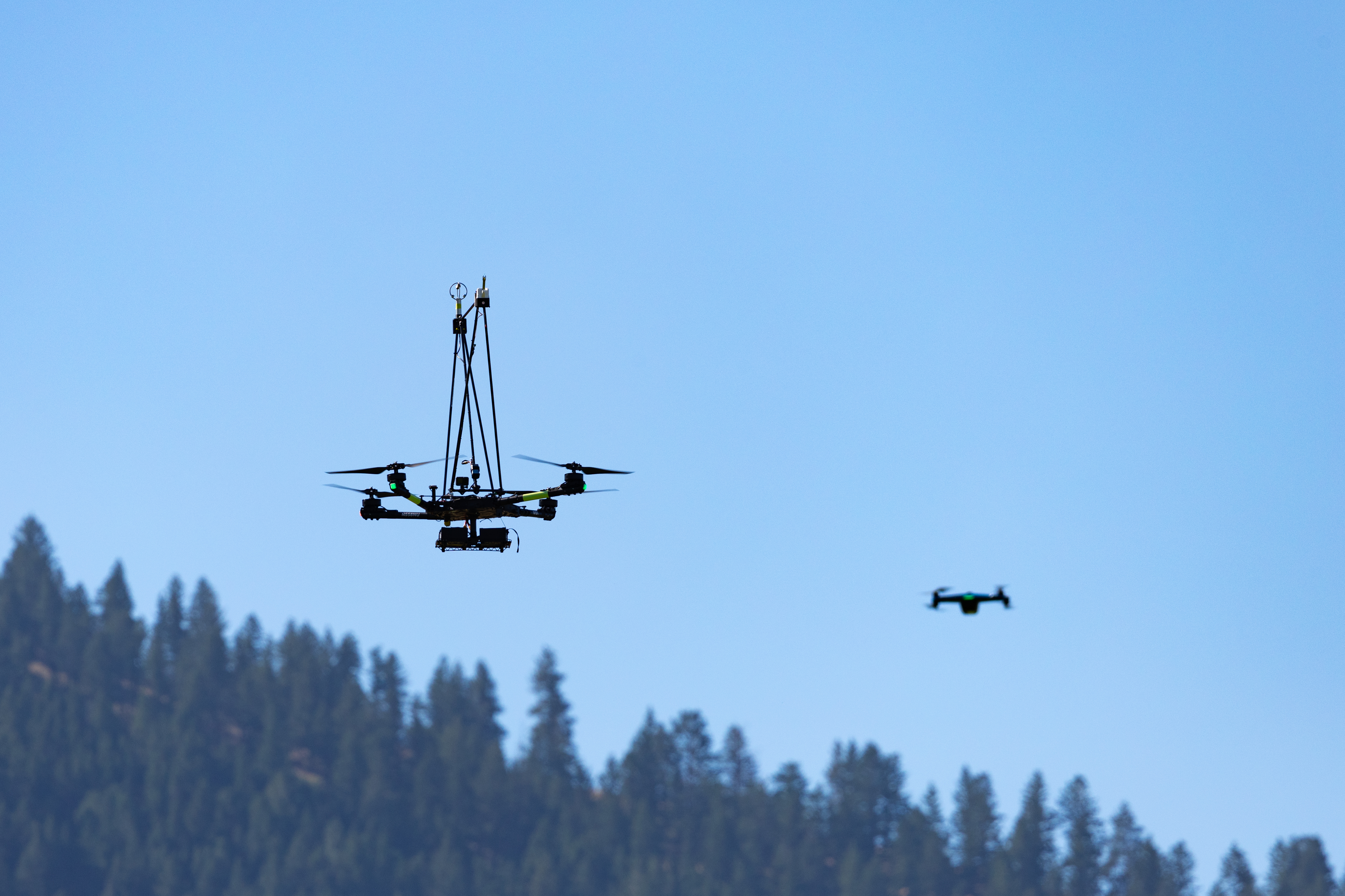 The NASA Alta X quadcopter and the Skydio-2 drone hover over the mountain during the final flight of the FireSense uncrewed aerial system (UAS) technology demonstration in Missoula, Montana.