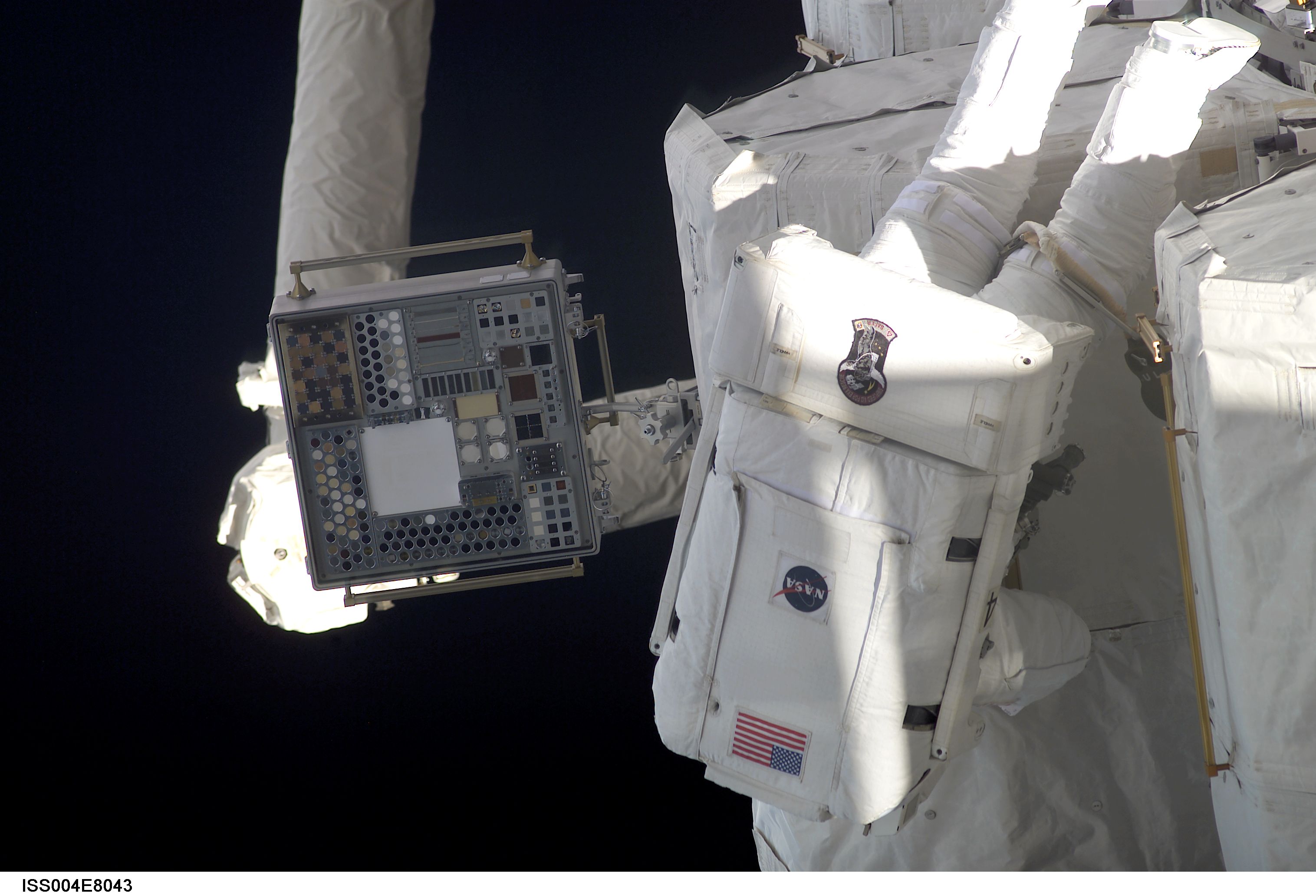 ISS004-E-8043 (20 February 2002) --- Astronaut Daniel W. Bursch, Expedition Four flight engineer, participates in the five-hour, 47-minute space walk on February 20, 2002. He moves among the oxygen and nitrogen tanks on the exterior of Quest Airlock. The square device (left) on the Space Station Remote Manipulator System (SSRMS) or Canadarm2 is the Materials International Space Station Experiment (MISSE). The image was recorded with a digital still camera.