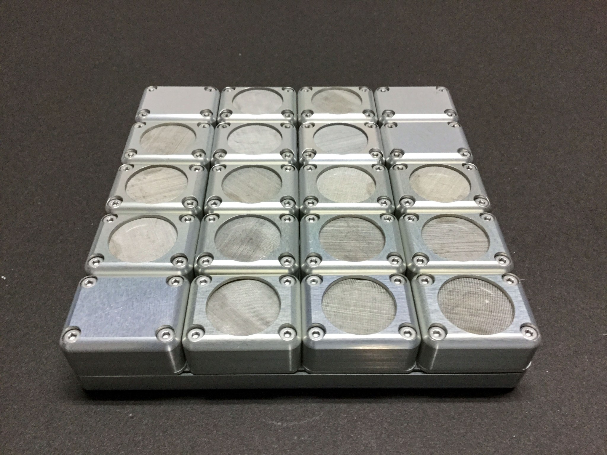 Grid of metallic square enclosures, each containing a circular opening, arranged in a compact layout against a dark background.