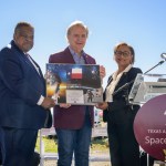 Three individuals pose during a presentation at the Texas A&M University Space Institute event. The person in the center holds a framed certificate featuring the Texas state flag and space exploration imagery.