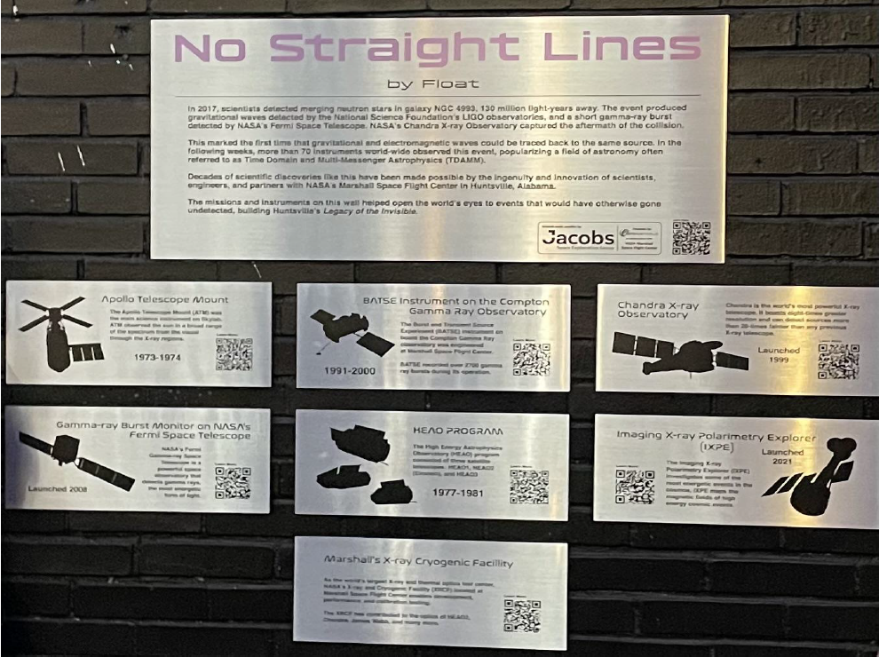 A photo of several silver plaques on a black brick wall.