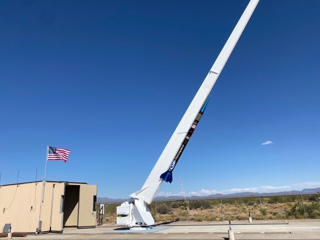 A black rocket is attached to an angled white rail awaiting launch.