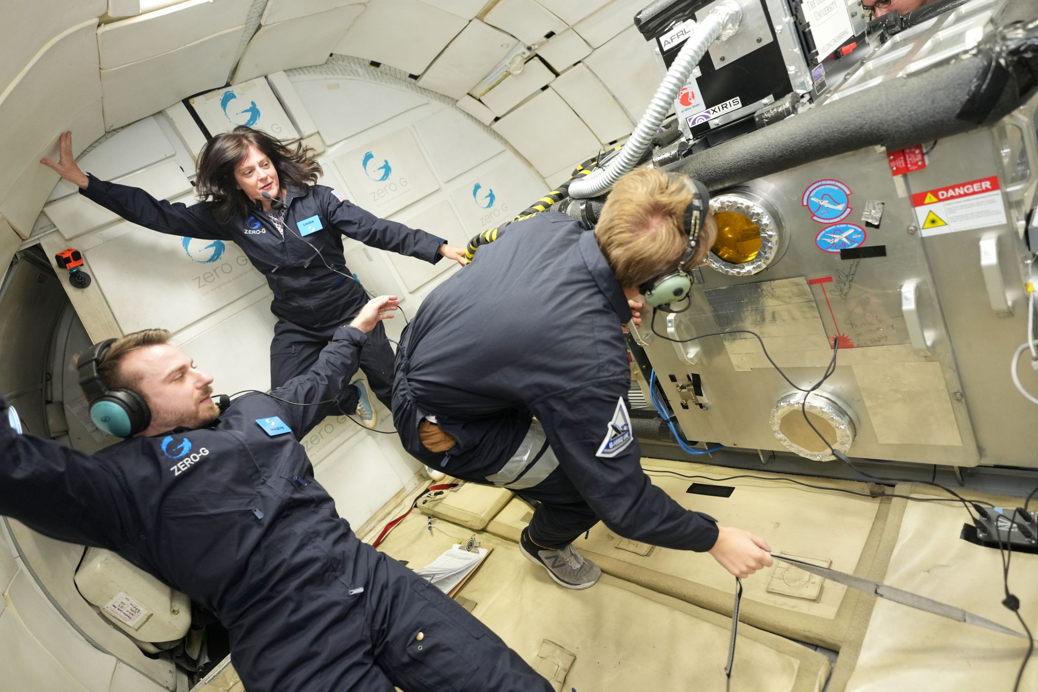 Three people float inside a vacuum chamber on an airplane.
