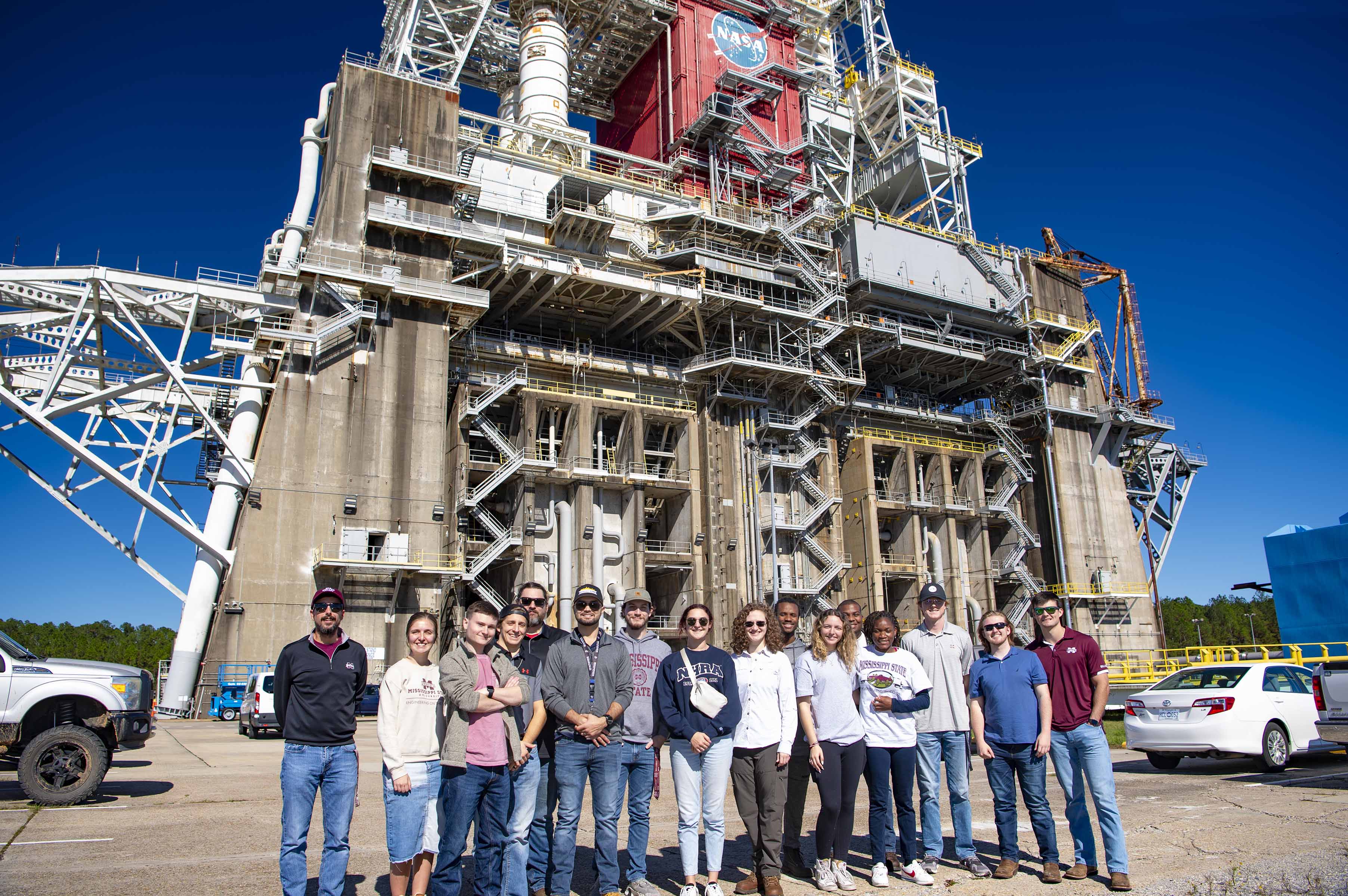 a group of college students pose for a photo in front of the Thad Cochran Test Stand while touring key facilities at NASA Stennis