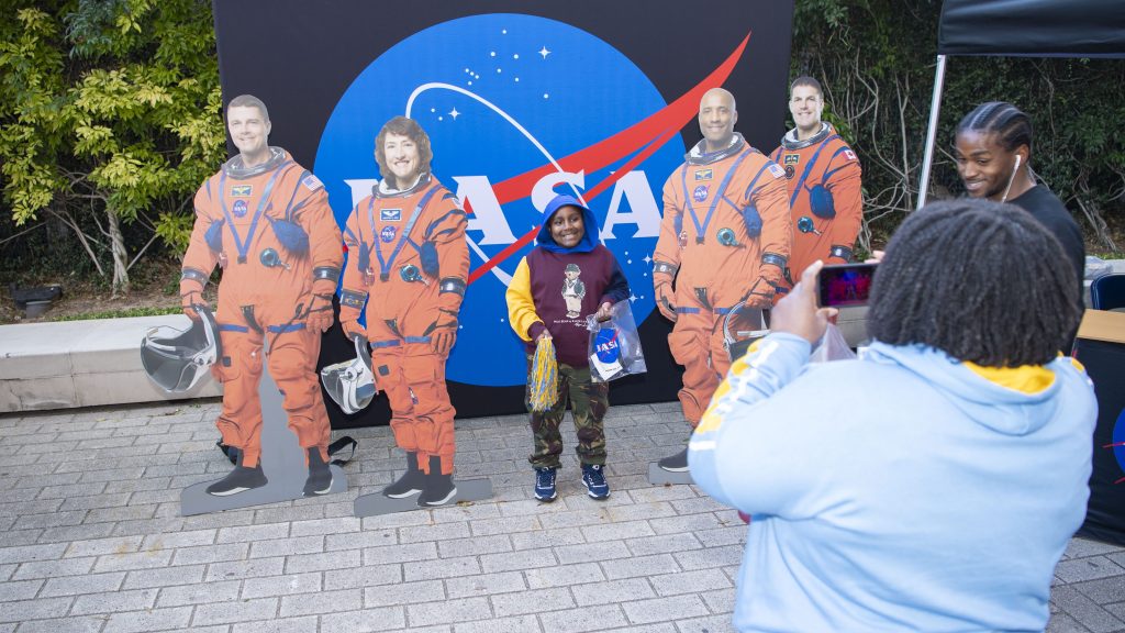 a young fan poses for a photo with cardboard images of NASA’s Artemis II crew