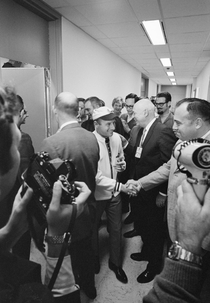 Black and white image of two men shaking hands, surrounded by a group of men