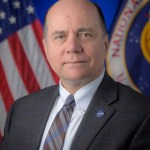 Official portrait of David Mitchell with American and NASA flag in the background