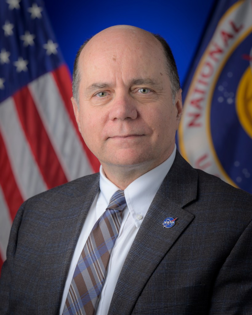 Official portrait of David Mitchell with American and NASA flag in the background